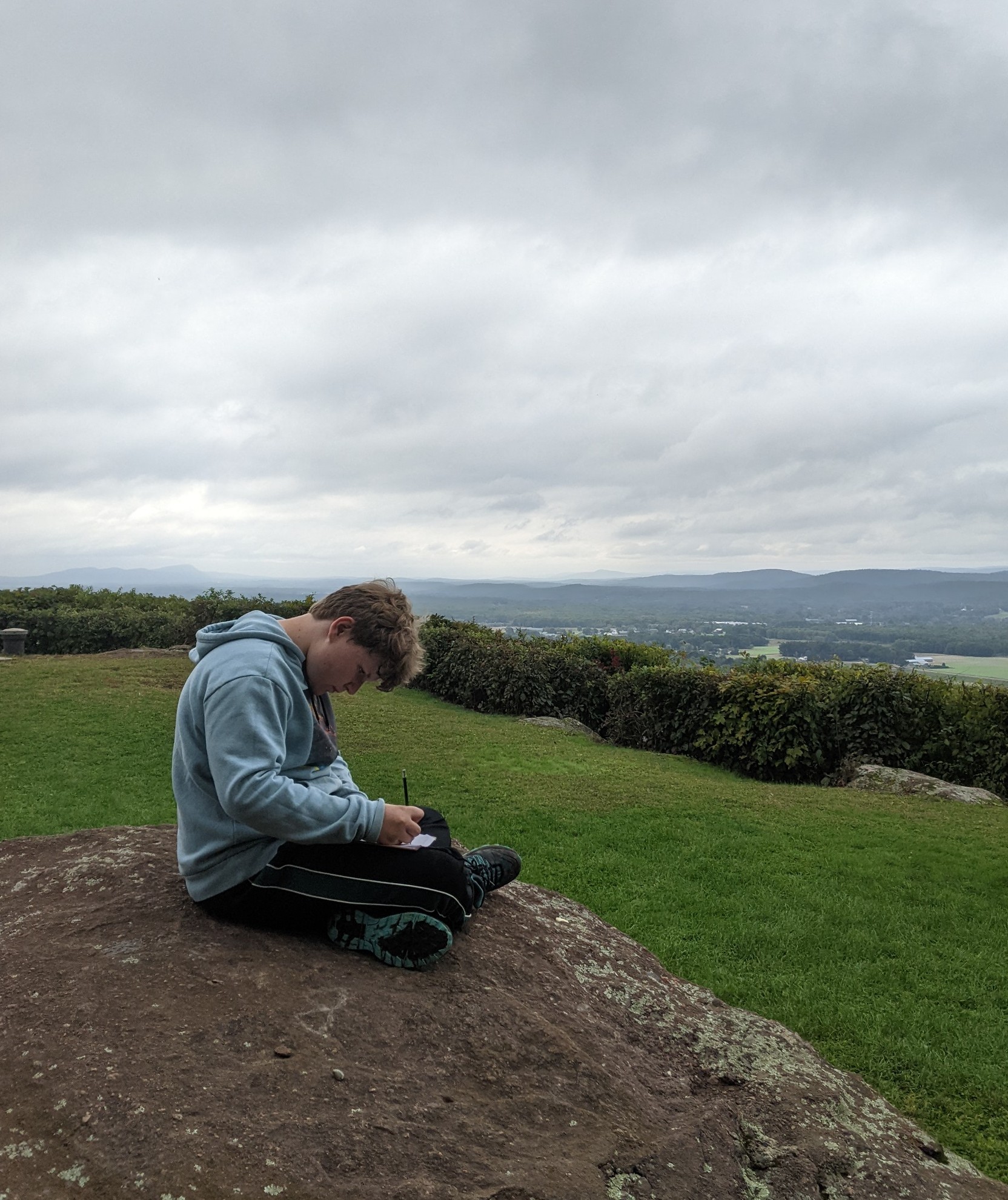 A student sits on a rock, writing