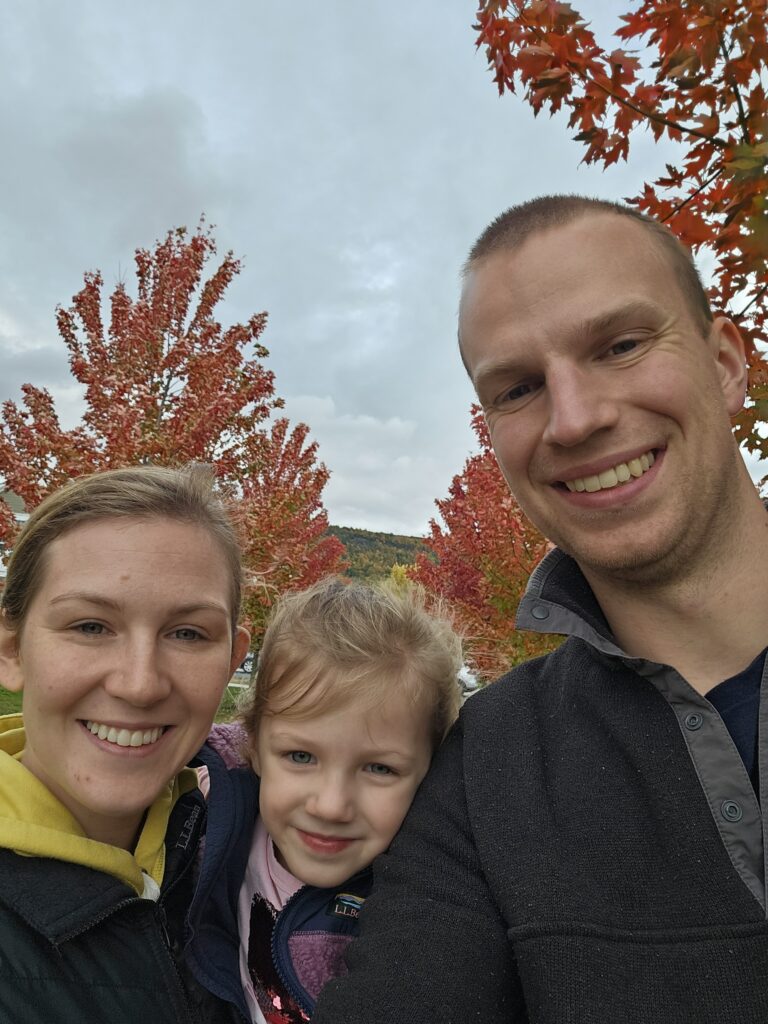 Nick, Chelsea, and their daughter smile at the camera