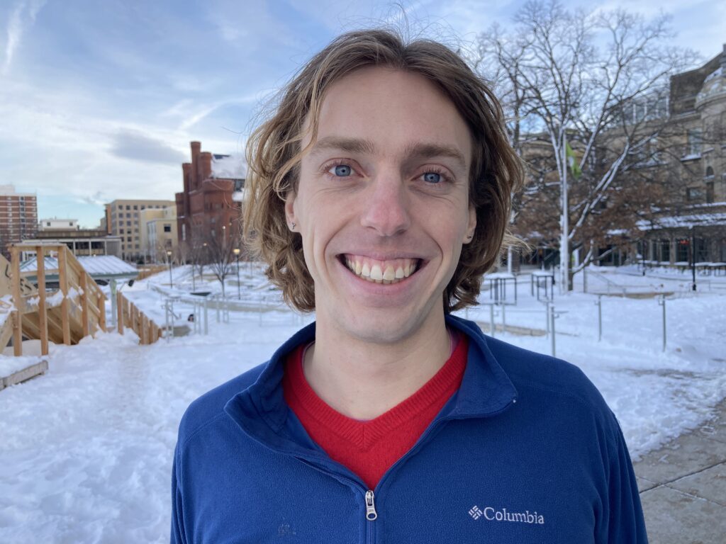 Kai DeLorenzo stands against a snowy backdrop, smiling at the camera